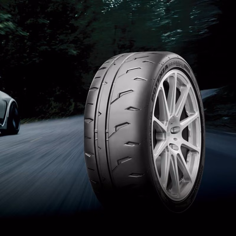 A performance tire on a silver alloy wheel, with a blurred car speeding along a dark road through trees.