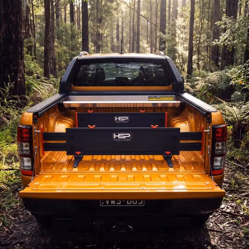 Rear view of an orange pickup truck in a forest, with a black HSP divider system fitted in the open tray.