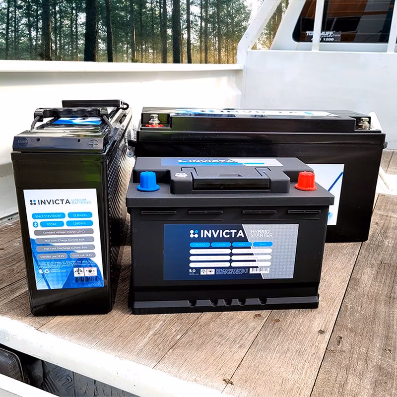 Three black Invicta batteries, including a lithium battery and a hybrid starter battery, on a wooden deck.