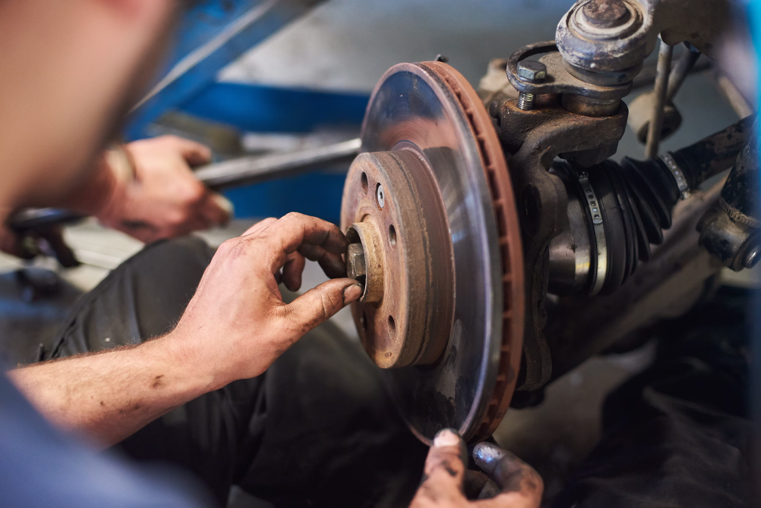 A mechanic's hands fitting a new brake disc and hub onto a car's wheel assembly in a workshop.