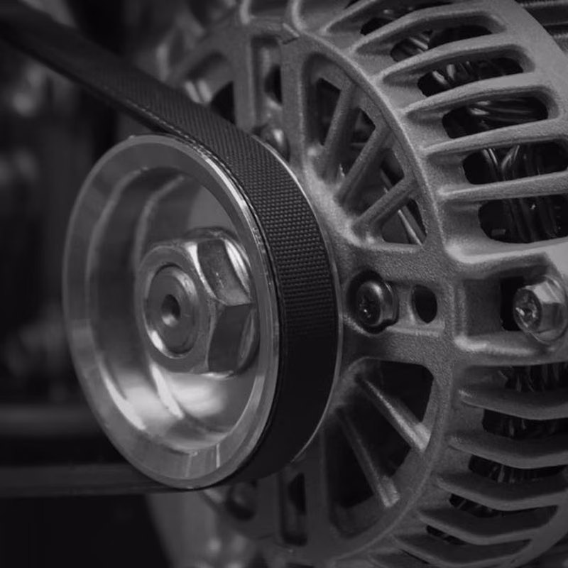 Close-up black and white view of a car alternator's metal pulley with a ribbed drive belt wrapped around it.